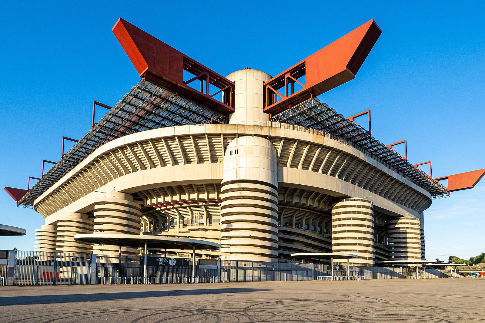 Het grote San Siro-stadion in Milaan met ronde torens en rode dakbalken onder een blauwe lucht.
