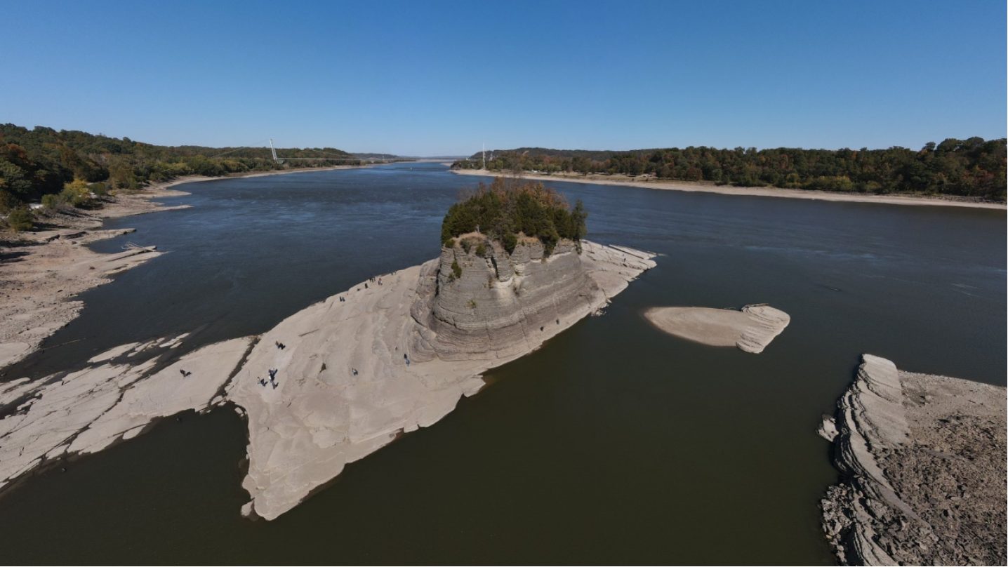 Luchtfoto van een brede rivier met laag water, waardoor een rotseiland en zandbanken droog liggen.