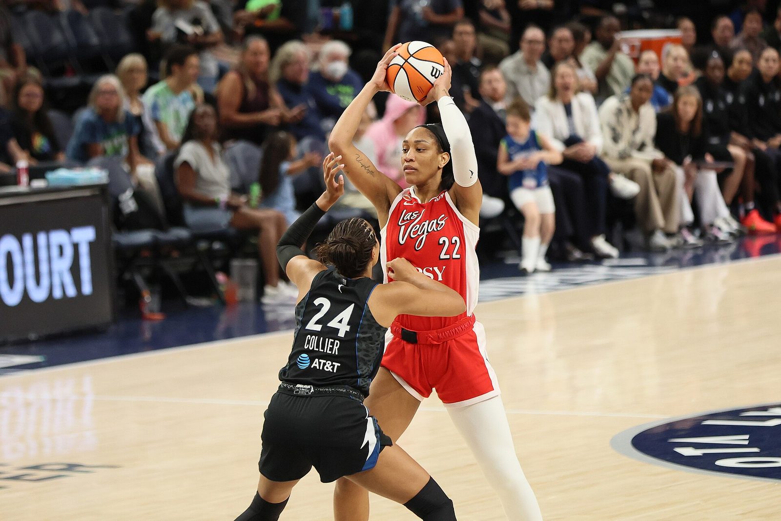 Een basketbalspeelster in een rood Las Vegas-shirt houdt de bal omhoog terwijl een tegenstandster in zwart verdedigt.