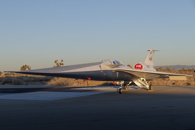 Het smalle, spitse X-59-vliegtuig van NASA staat bij zonsopkomst op het platform in de woestijn.