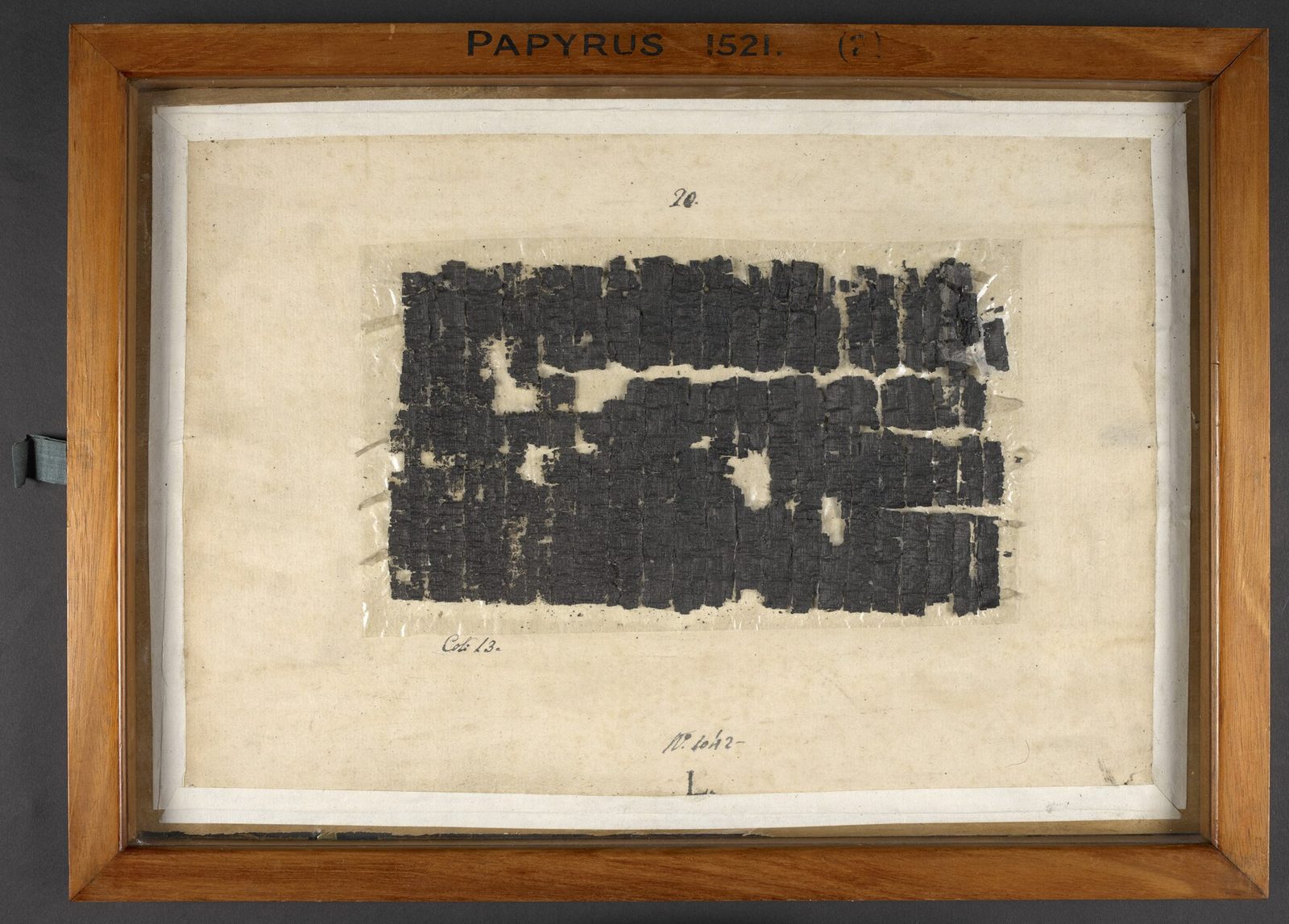 Een donker, verkoold stuk oude papyrus achter glas in een houten lijst.