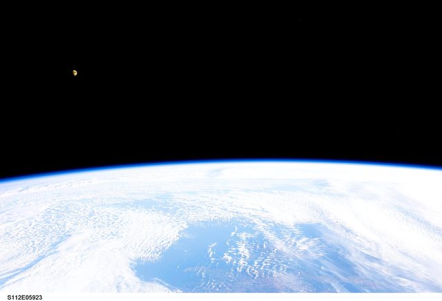 Vanuit de ruimte zie je de gebogen aarde met wolken boven de Atlantische Oceaan en een kleine maan in het donker.