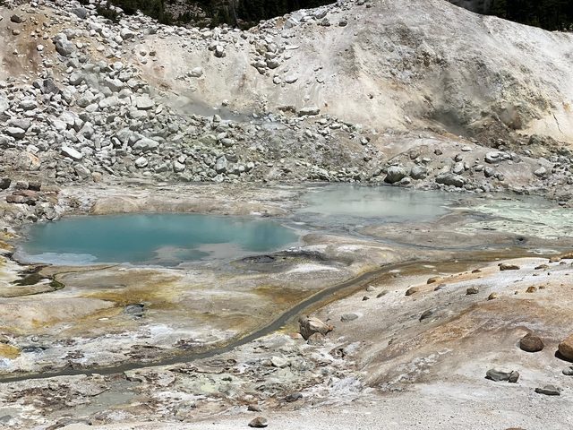 Turquoiseblauwe poelen met warm water tussen lichte rotsen en gele bodem in een vulkanisch gebied.