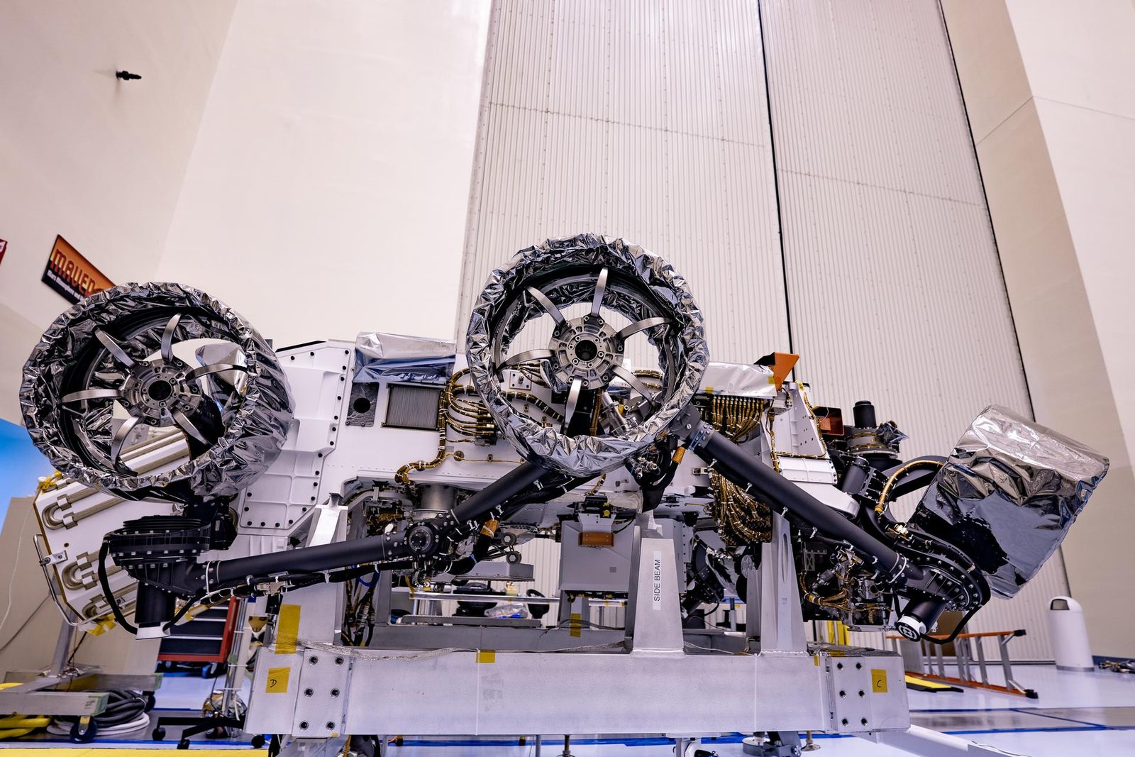 De Nasa-rover Perseverance staat in een grote hal met zijn wielen met zilverkleurige folie eraan gemonteerd.