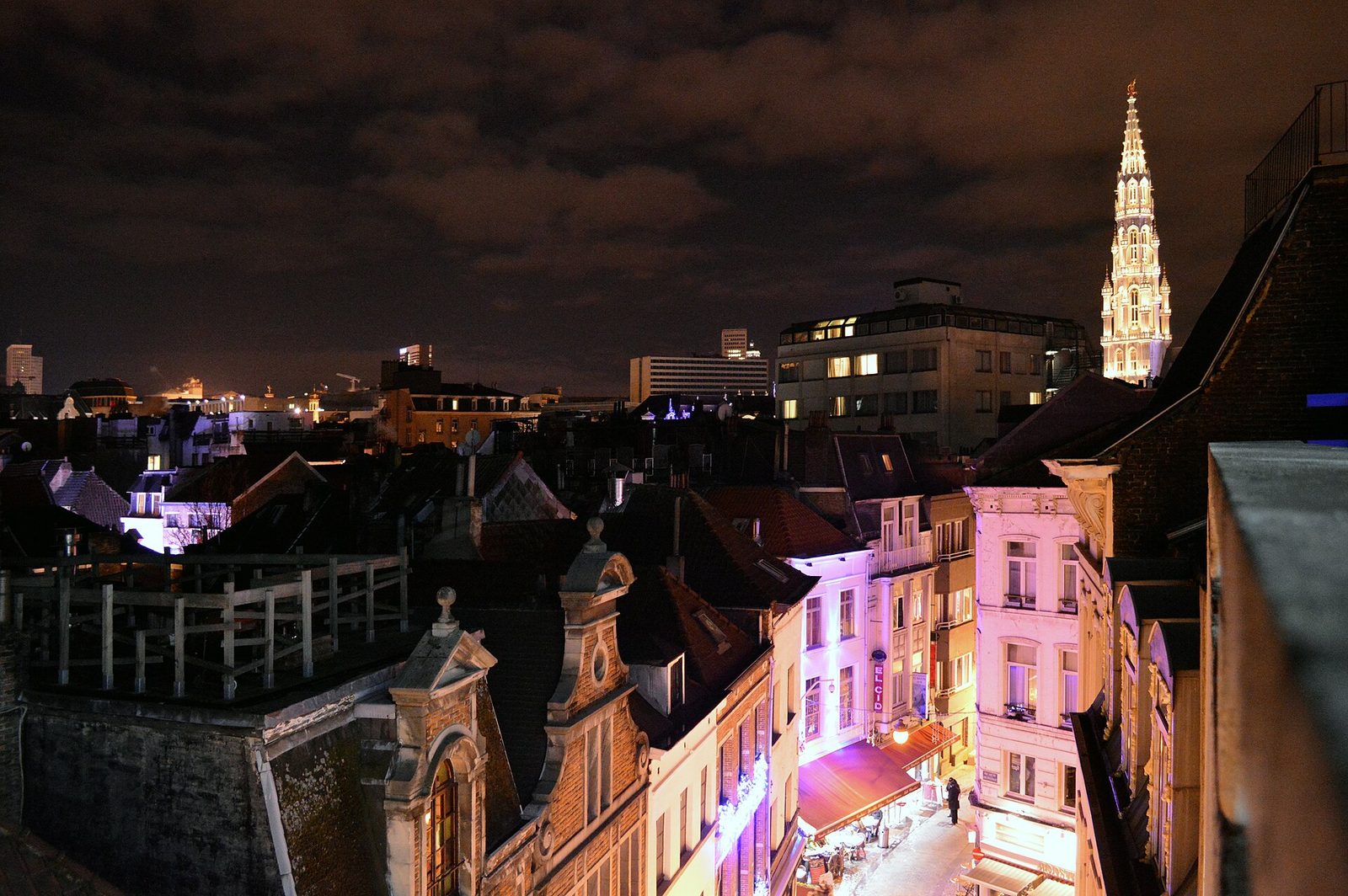 Nachtelijk uitzicht over de daken van Brussel met links een straat met lichtjes en rechts een hoge verlichte toren.